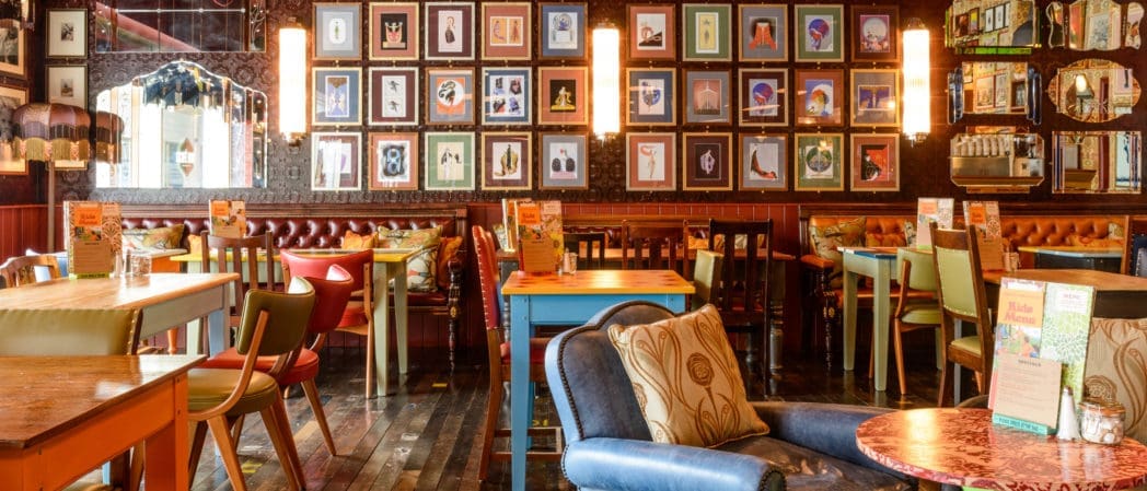 Colorful Centro restaurant interior with eclectic furniture, wooden tables, cushioned chairs, and couches. Walls are decorated with framed artwork and ornate mirrors, while warm lighting creates a cozy atmosphere.