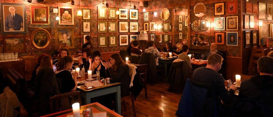 A cozy restaurant with dim lighting, candles on tables, and people dining. The walls are decorated with numerous framed pictures and mirrors, creating Clavio’s signature warm, inviting atmosphere.