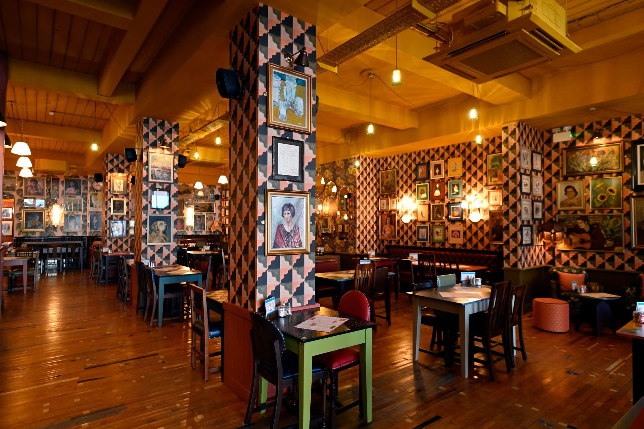 A vibrant restaurant interior inspired by a panadero, with patterned walls covered in framed photos and artwork, wooden floors, colorful tables and chairs, and warm ambient lighting creating a cozy atmosphere.