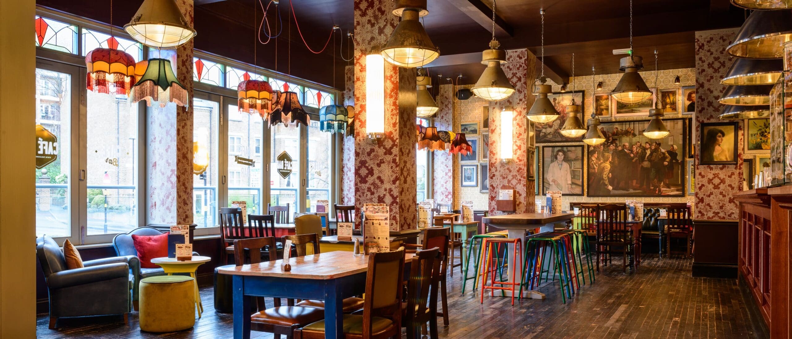Quinto is a cozy, eclectic restaurant with floral wallpaper, wooden tables and chairs, colorful stools, vintage hanging lamps, and framed artwork on the walls. Large windows fill Quinto with natural light.