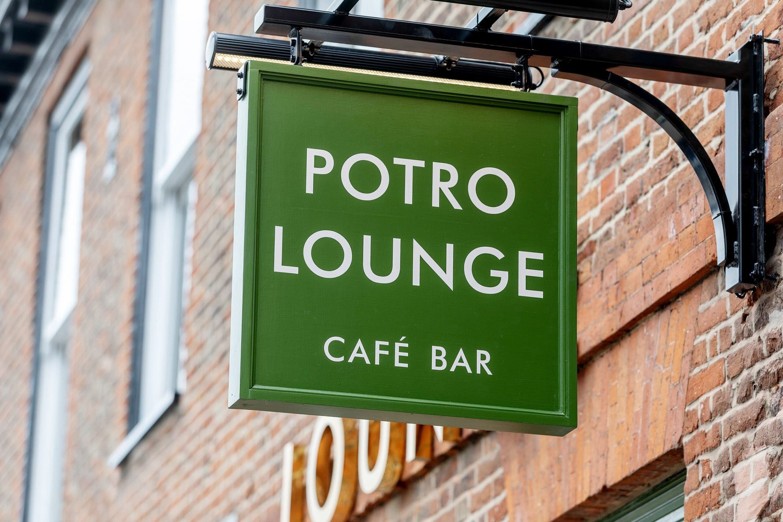 A green sign with white text reading "POTRO LOUNGE CAFÉ BAR" hangs outside a brick building, inviting guests to experience the unique charm of Potro.