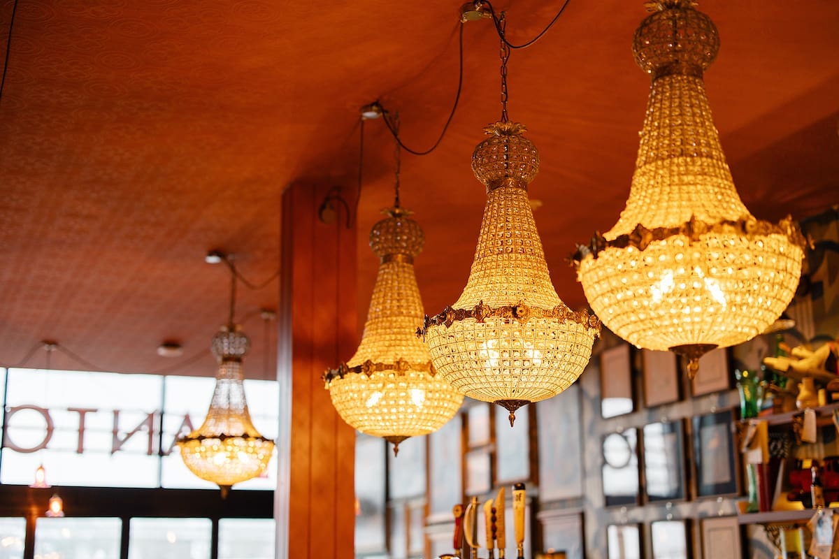 Four ornate crystal chandeliers hang from the ceiling in Cantoro’s warmly lit interior, creating a cozy atmosphere. Framed pictures and decor items are visible on the wall in the background.